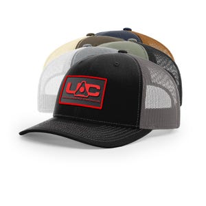May include: A collection of trucker hats in various colors, including black, gray, tan, and navy. The front of the black hat features a red rectangular patch with the letters "LAC" and the words "UNION AEROSPACE CORPORATION".