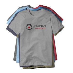 May include: A stack of gray, blue, and red crew neck t-shirts. The front shirt is gray with the text "VERIDIAN DYNAMICS" printed in black and red. The logo is a black circle with a red triangle inside.