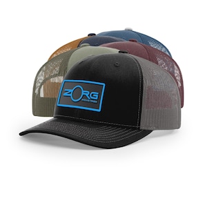 May include: A collection of trucker hats in various colors, including black, brown, and blue. The front of the black hat features a blue rectangular patch with the text "ZORG INDUSTRIES". The hats have mesh backs and curved brims.