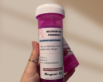 Może przedstawiać: Różowa plastikowa butelka na tabletki z białym korkiem i etykietą z napisem "Recovery Kit Pharmacy" w chorobie i zdrowiu. Etykieta zawiera również napis "Przyjmować w razie potrzeby w celu złagodzenia kaca". Butelka ma numer recepty i napis "Hangover Kit" na spodzie.