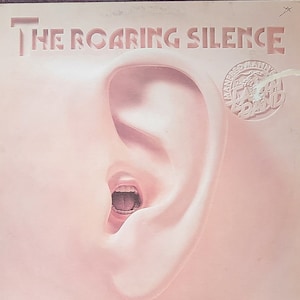 Peut inclure: Une pochette d'album vinyle rose avec le titre "The Roaring Silence" et une image d'une grande oreille avec une bouche ouverte à l'intérieur. L'album est du groupe "The Mannish Boys".