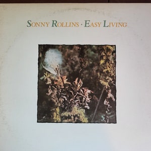 Op de afbeelding: Een vintage vinyl platenhoes met een close-up van een witte paardenbloemzaadkop met een wazige achtergrond van groen en bruin gebladerte. De albumtitel "SONNY ROLLINS - EASY LIVING" is gedrukt in groene en bruine tekst bovenaan de hoes.