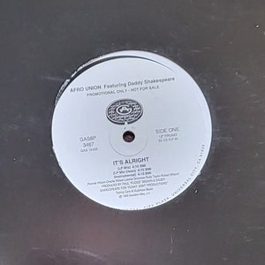 May include: A black vinyl record with a white label. The label has the text "AFRO UNION Featuring Daddy Shakespeare", "PROMOTIONAL ONLY - NOT FOR SALE", "GASSP 3467", "SIDE ONE", "IT'S ALRIGHT", and "LP Mix - 4:18  Edit - 3:58".