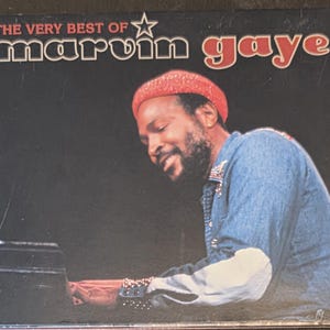 May include: Album cover for "The Very Best of Marvin Gaye." The image features a smiling man wearing a red hat and denim shirt, playing a piano. The album title is in white and red text against a black background.