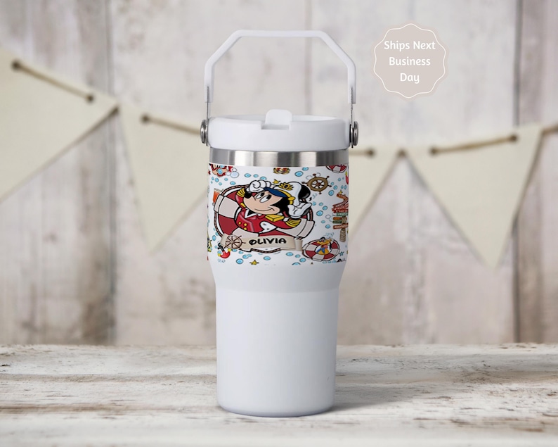 May include: A white insulated tumbler with a handle and a stainless steel band. The tumbler features a colorful wrap with a cartoon character in a nautical theme, with the name "Olivia" on it. The tumbler has a white lid.