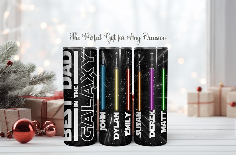 K&ouml;nnte beinhalten: Drei schwarze isolierte Becher mit Weltraum-Motiv. Auf einem Becher steht "BEST DAD IN THE GALAXY" mit einem Lichtschwert-Design. Die anderen beiden Becher haben Lichtschwerter in Blau, Gelb, Rot, Lila und Gr&uuml;n mit Namen.