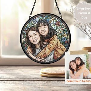 May include: A round stained glass window art piece featuring two smiling women embracing. The artwork is framed in black and hangs from a chain. The background includes colorful floral designs. A small photo with the text "Send Your picture" is also visible.