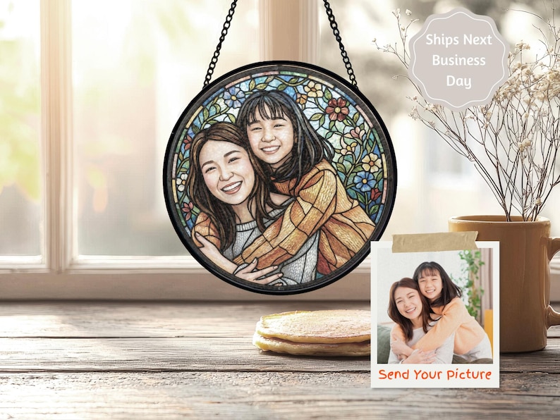 May include: A round stained glass window art piece featuring two smiling women embracing. The artwork is framed in black and hangs from a chain. The background includes colorful floral designs. A small photo with the text "Send Your picture" is also visible.