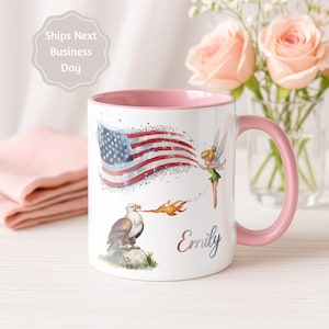 Könnte beinhalten: Weiße Keramiktasse mit rosa Griff und Innenraum. Die Tasse zeigt ein Design der amerikanischen Flagge, einen Adler und eine Fee. Der Name "Emily" steht auf der Tasse. Die Tasse ist mit patriotischen Bildern verziert.