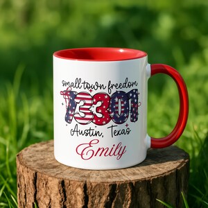 Op de afbeelding: Een witte keramische mok met een rode binnenkant en handvat. De voorzijde toont de tekst "small town freedom" boven het getal "73301" in een patriottisch vlagpatroon, gevolgd door "Austin, Texas" en de naam "Emily" in een rood handschrift.