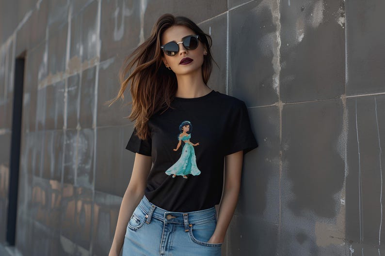 May include: Black t-shirt featuring a watercolor illustration of a princess in a teal gown. The graphic tee has short sleeves and a crew neck. The model is wearing blue jeans and sunglasses.