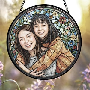 May include: Round stained glass art piece featuring two smiling women embracing. The artwork is framed in black and has a colorful floral border. The women are depicted in a warm, inviting style, with a soft, painterly effect.