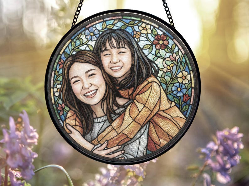 May include: Round stained glass art piece featuring two smiling women embracing. The artwork is framed in black and has a colorful floral border. The women are depicted in a warm, inviting style, with a soft, painterly effect.