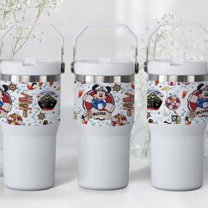 May include: Three white insulated tumblers with a handle. Each tumbler features a nautical-themed design with Mickey Mouse, a cruise ship, and other nautical elements. The name "Oliver" is printed on one of the tumblers.