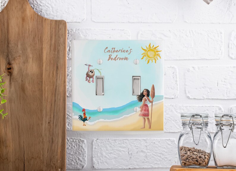 May include: A double light switch cover featuring a beach scene with a cartoon girl holding a wooden oar, a rooster, and a small creature hanging from a vine. The text Catherine's Bedroom is printed at the top with a yellow sun illustration.