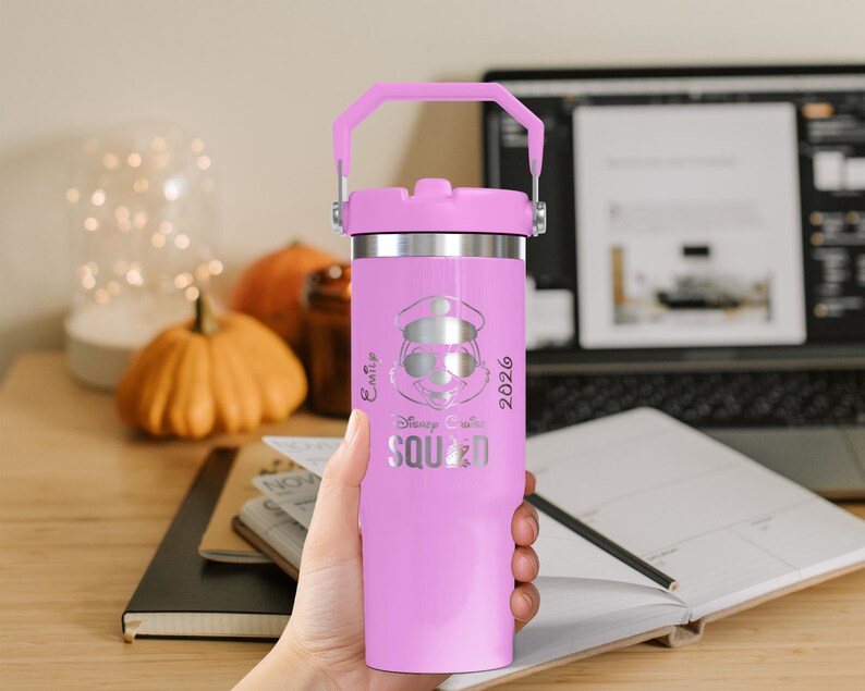Puede incluir: Un vaso t&eacute;rmico rosa con borde y asa plateados. El vaso presenta un grabado plateado de un personaje de dibujos animados con sombrero y gafas de sol, con las palabras "Disney Cruise Squad 2026".