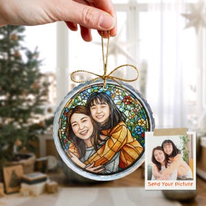 May include: A round, clear glass ornament with a stained-glass design featuring a portrait of two people hugging. The ornament has a gold string for hanging and a small photo with the text "Send Your Picture".