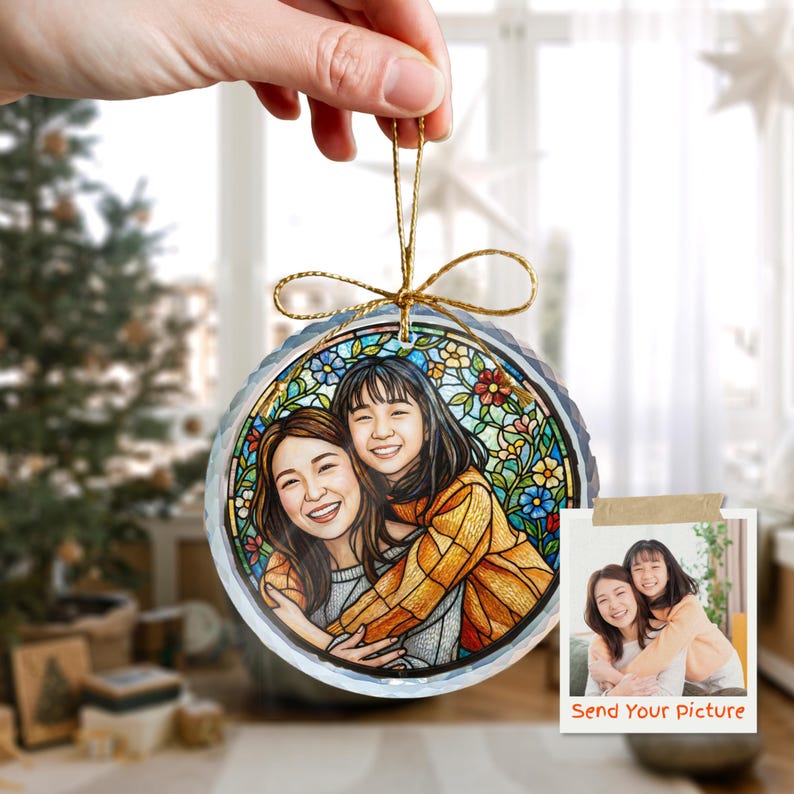 May include: A round, clear glass ornament with a stained-glass design featuring a portrait of two people hugging. The ornament has a gold string for hanging and a small photo with the text "Send Your Picture".