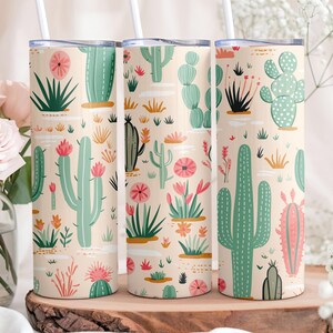 May include: Three cylindrical tumblers with lids and straws, featuring a repeating pattern of various green cacti and pink flowers on a light beige background. The design includes saguaro, prickly pear, and barrel cacti in shades of green.