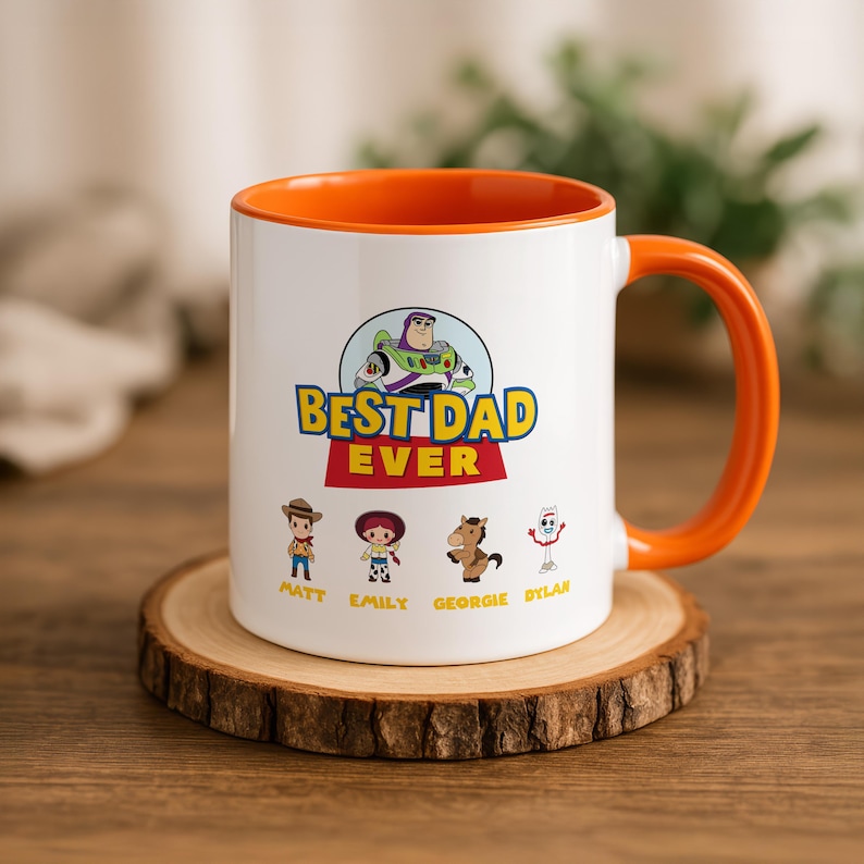 May include: A white ceramic mug with an orange interior and handle. The front features a graphic of Buzz Lightyear above the text "BEST DAD EVER" and four Toy Story characters with the names "MATT," "EMILY," "GEORGIE," and "DYLAN" printed below.