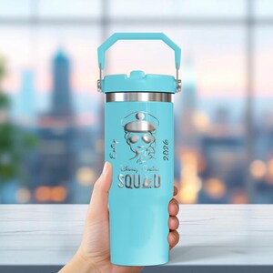 Puede incluir: Un vaso aislado azul claro con asa, borde y tapa plateados. El vaso presenta un gr&aacute;fico de un personaje con sombrero y gafas de sol, con el texto "Party Squad 2026" y "Disney Cruise".