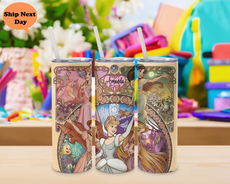 Op de afbeelding: Drie roestvrijstalen bekers met een cr&egrave;mekleurige achtergrond en afbeeldingen van Disney-prinsessen. De prinsessen zijn Assepoester, Rapunzel en Jasmine. De bekers hebben een gouden rand en het woord "Amanda" staat op een van de bekers.