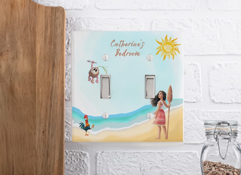 May include: A double light switch plate featuring a beach scene with a yellow sun, a cartoon coconut character, a rooster, and a girl holding a wooden oar. The text Catherine's Bedroom is printed in brown script at the top of the white plastic cover.
