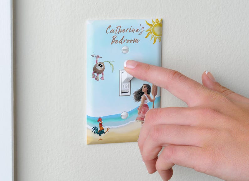 May include: A rectangular light switch cover plate featuring a Moana-themed design with a beach scene, a rooster, a small creature, and a yellow sun. The text "Catherine's Bedroom" is printed at the top in brown script. The plate is white with two screws.