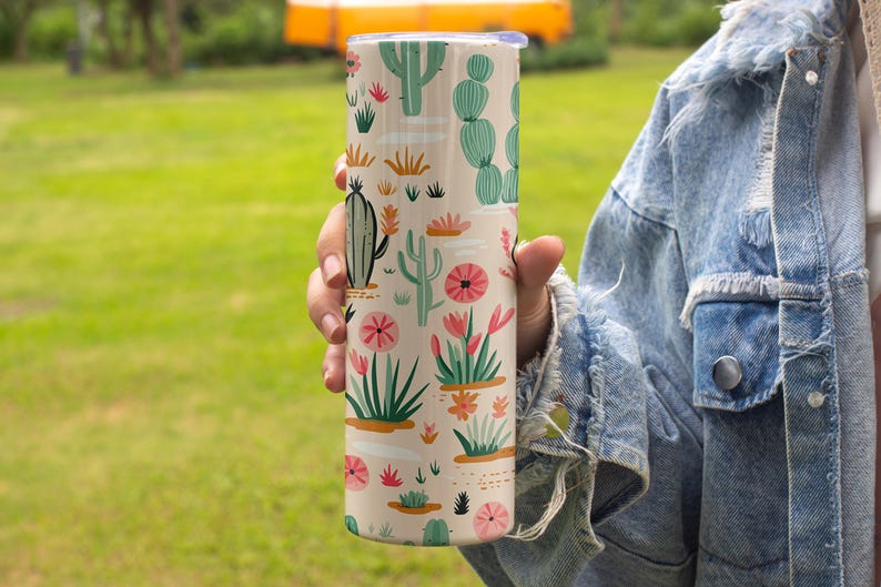 May include: A cylindrical tumbler with a light beige background featuring a repeating pattern of various green cacti and succulents, interspersed with small pink and orange flowers and white horizontal dashes across the entire surface.