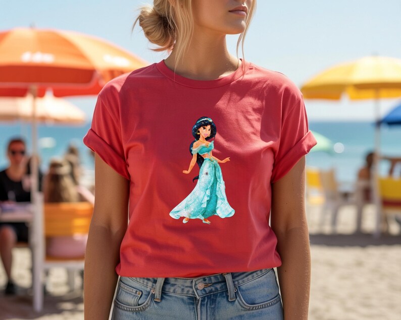 May include: A red t-shirt featuring a graphic of a cartoon princess in a turquoise dress. The shirt has rolled-up sleeves and is paired with blue jeans. The background shows a beach scene with umbrellas and the ocean.