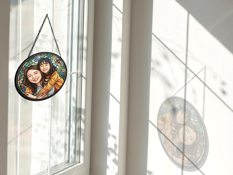 May include: A round stained glass window hanging from a black chain. The window features a portrait of two people, with a colorful floral background. The window is hanging in front of a window.