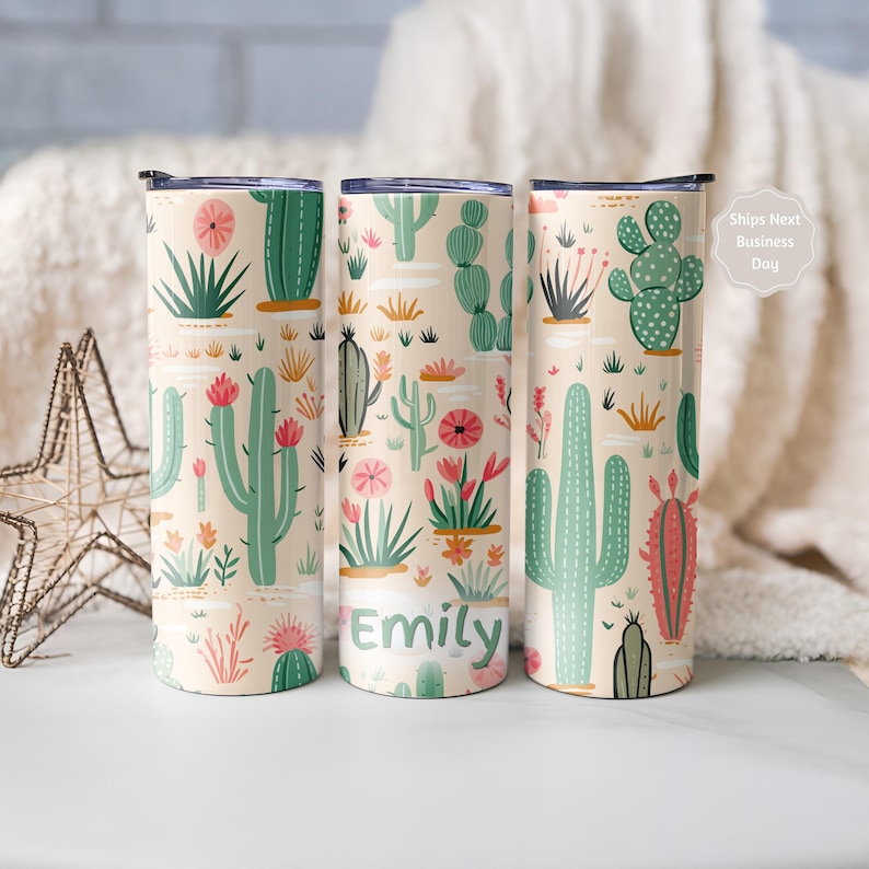 May include: Three cylindrical tumblers with a light beige background featuring a repeating pattern of green and pink cacti and desert plants. The center tumbler includes the name Emily printed in green letters near the bottom of the design.