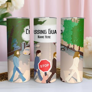 Könnte beinhalten: Drei zylindrische Becher mit einer farbenfrohen Illustration einer Straßenszene. Das Design zeigt Figuren, die einen Zebrastreifen überqueren, mit dem Text "Crossing Guard" und "Name Here". Die Becher sind mit einem grünen und beigen Hintergrund verziert.