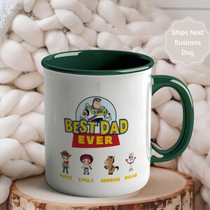 May include: A white ceramic mug with a dark green interior and handle. The front features a graphic of Buzz Lightyear above the text "BEST DAD EVER" in yellow and red. Below are four cartoon characters with the names Matt, Emily, Georgie, and Dylan.
