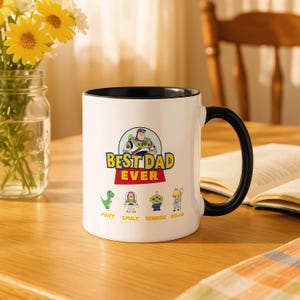 May include: A white ceramic mug with a black handle and interior featuring a graphic of Buzz Lightyear above the text BEST DAD EVER. Below the text are four small character illustrations with the names Matt, Emily, Georgie, and Dylan printed below.