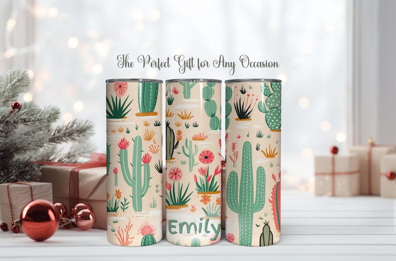 May include: Three cylindrical tumblers with a light beige background featuring a repeating pattern of green cacti and pink flowers. The center tumbler displays the name Emily in green text. Each tumbler has a metallic rim at the top and bottom.