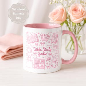 May include: A white ceramic mug with a pink interior and handle, featuring pink line art illustrations of a Bible, pens, a journal, a tote bag, a bookshelf, and a chair, with the text "Bible Study Girlie" printed in the center.