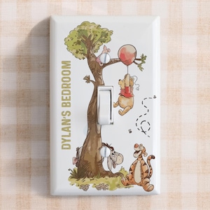 May include: White light switch cover with a colourful illustration of Winnie the Pooh characters. The design includes Pooh Bear with a balloon, Tigger, Eeyore, and Piglet. The text "DYLAN'S BEDROOM" is printed vertically in gold.