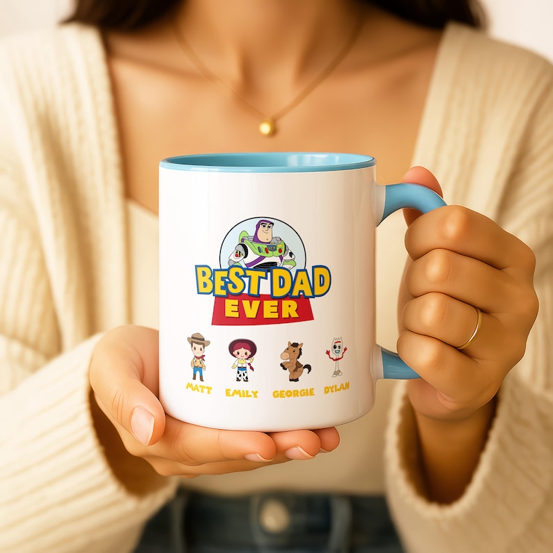 May include: A white ceramic mug with a light blue interior and handle. The front features a graphic of Buzz Lightyear above the text BEST DAD EVER, followed by four Toy Story character illustrations with the names Matt, Emily, Georgie, and Dylan.