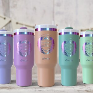 May include: Five insulated tumblers in pastel colors: lavender, purple, peach, teal, and mint green. Each tumbler has a white lid with a silver band, a straw, and a handle. The tumblers are decorated with a shield design and the text "Guarded by Heaven" and "Emily".