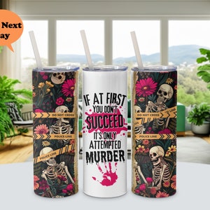 May include: Three stainless steel tumblers with different designs. The first tumbler has a floral and skeleton design with the text "DO NOT CROSS" and "POLICE LINE". The second tumbler has the text "IF AT FIRST YOU DON'T SUCCEED IT'S ONLY ATTEMPTED MURDER" with a pink handprint. The third tumbler has a floral and skeleton design with the text "DO NOT CROSS" and "POLICE LINE".