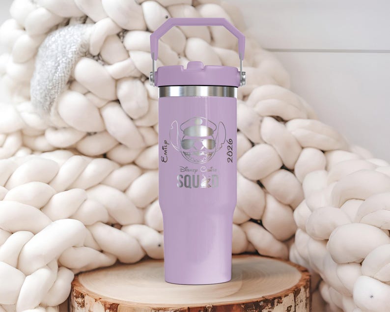 Puede incluir: Un vaso aislado de color lavanda con un borde plateado y un asa a juego. El vaso presenta un gr&aacute;fico de un personaje con gafas de sol y un sombrero, con el texto "Disney Ohana Squad 2026". El vaso est&aacute; sobre una superficie de madera.