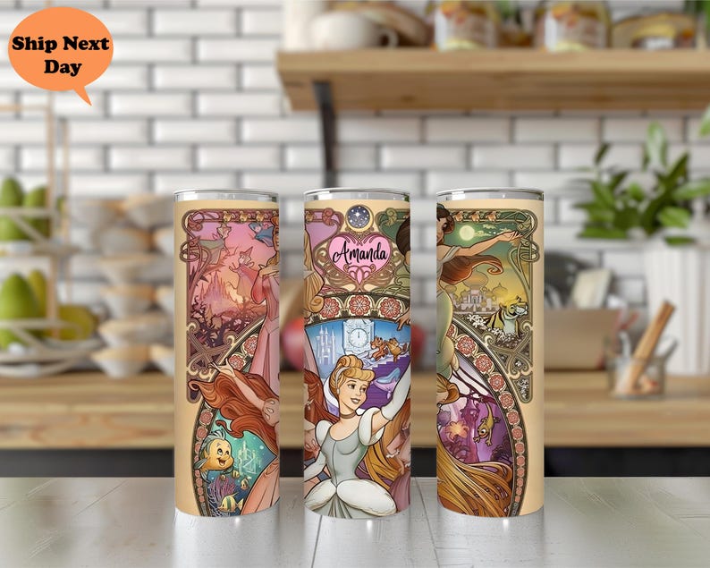 Op de afbeelding: Drie roestvrijstalen bekers met een kleurrijk ontwerp met prinsessen uit Disney's Assepoester. De bekers hebben een gouden rand en een doorzichtig deksel. Het ontwerp bevat een kasteel, een klok en een koets. De tekst "Amanda" staat op een van de bekers.