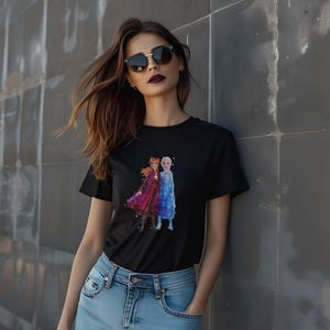May include: Black t-shirt featuring a watercolor image of two animated characters in red and blue dresses. The t-shirt is worn by a person wearing sunglasses and blue jeans.