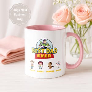 May include: A white ceramic mug with a pink interior and handle, featuring a graphic of Buzz Lightyear above the text BEST DAD EVER. Below are four cartoon characters with the names Matt, Emily, Georgie, and Dylan printed underneath them.