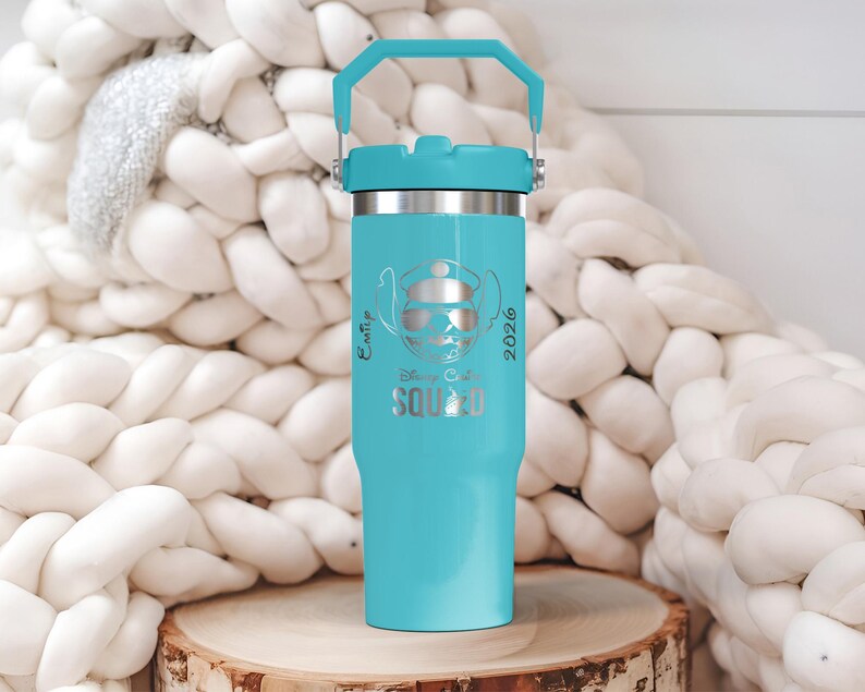 Puede incluir: Un vaso aislado turquesa con asa y borde plateado. El vaso presenta un dise&ntilde;o grabado con l&aacute;ser de un personaje de dibujos animados con sombrero y gafas de sol, con las palabras "Emp Disney Squad 2026". El vaso est&aacute; sobre una superficie de madera.