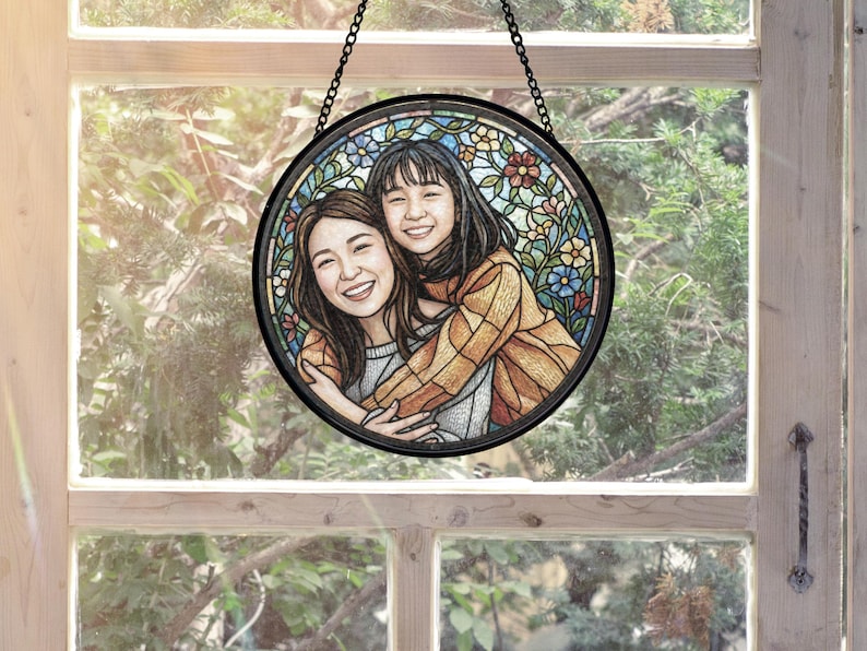 May include: A round, stained-glass window art piece featuring two smiling women embracing. The artwork is set against a backdrop of colorful floral patterns. The piece is framed in black and suspended by a chain, creating a decorative element.