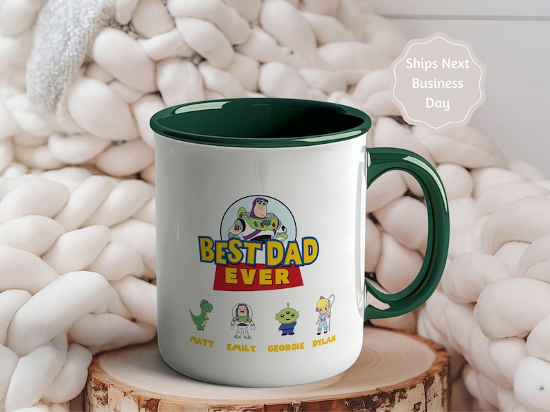 May include: A white ceramic mug with a dark green interior and handle. The front features a graphic of Buzz Lightyear above the text "BEST DAD EVER" and four small character illustrations with the names Matt, Emily, Georgie, and Dylan below.