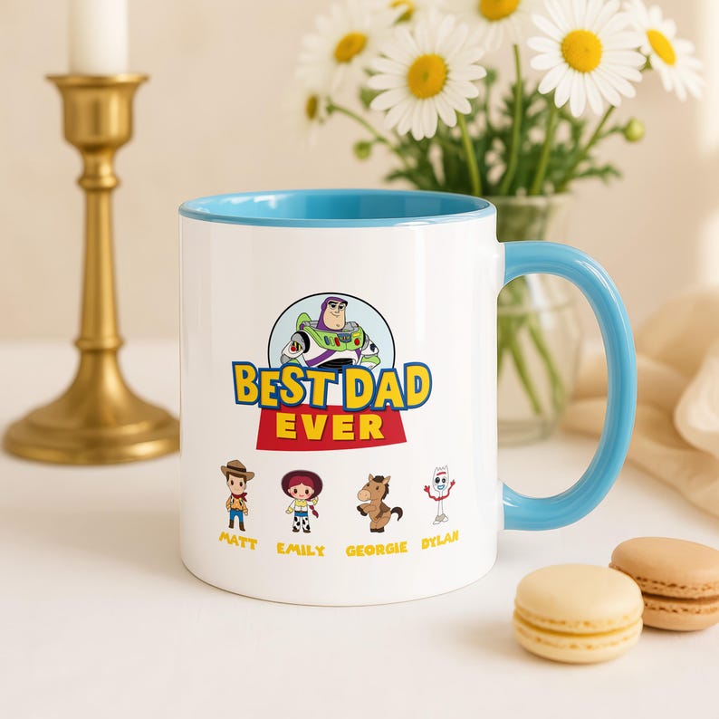May include: A white ceramic mug with a light blue interior and handle. The front features a graphic of Buzz Lightyear above the text BEST DAD EVER, followed by four cartoon characters labeled Matt, Emily, Georgie, and Dylan in yellow text.