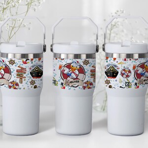 May include: Three white insulated tumblers with a handle. Each tumbler features a wrap-around design with nautical elements, including a cruise ship, Donald Duck in a life preserver, and the name "Oliver".